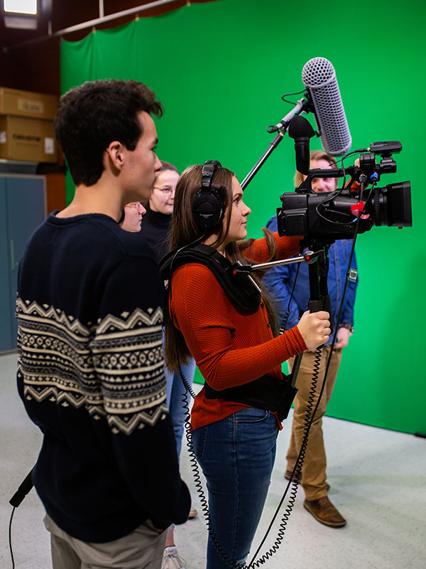Étudiants manipulant une caméra vidéo et des appareils de prise de son dans un studio.