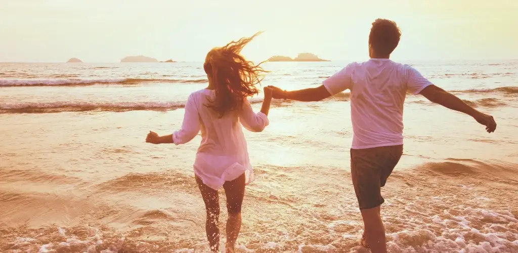 Couple se tenant par la main marchant sur la plage.