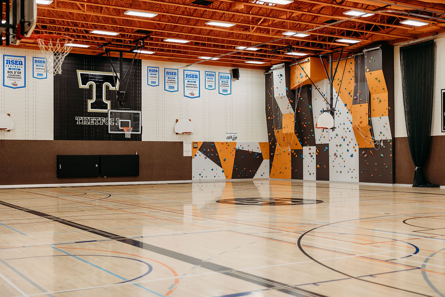 Photo du gymnase du Cégep de Thetford présentant les installations de basketball ainsi qu'un mur d'escalade.