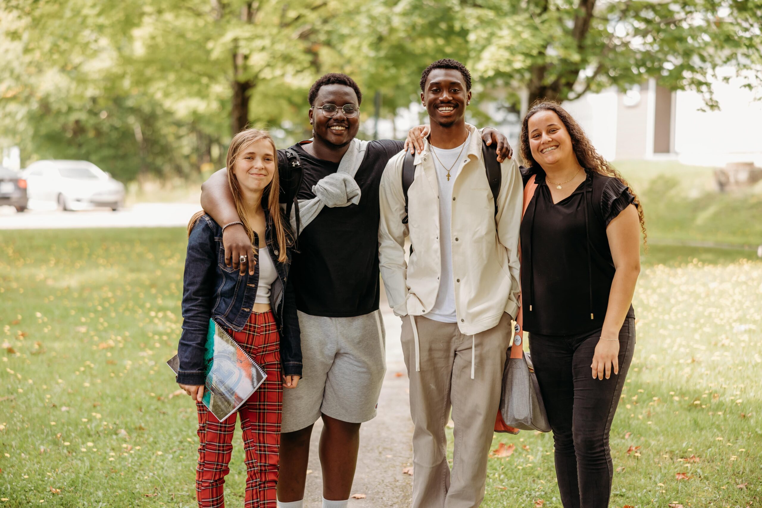 Quatre étudiants souriant à la caméra à l'extérieur