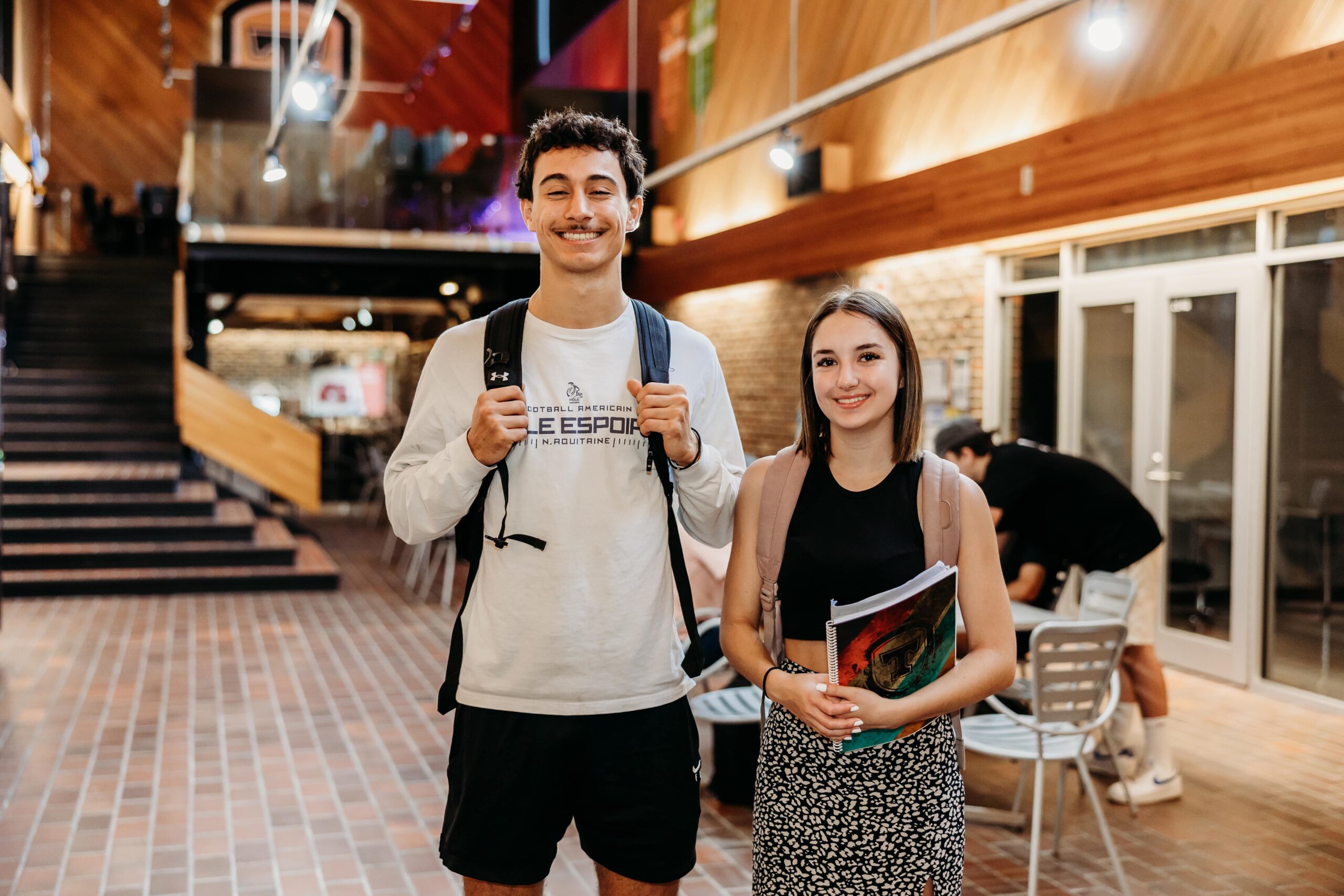 Deux jeunes étudiants sourient à la caméra dans un espace commun du Cégep de Thetford.